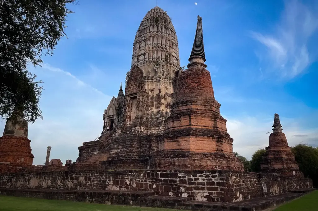 Ancient prang and surrounding chedis at Wat Ratchaburana in Ayutthaya Historical Park, Thailand, under a blue sky with scattered clouds.