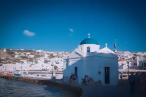 White Greek Orthodox church with blue dome overlooking the harbor and coastal village of Mykonos, Greece