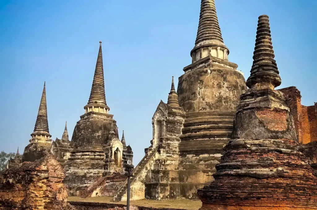 Ancient temple ruins and iconic stupas at Ayutthaya Historical Park in Ayutthaya, Thailand, showcasing centuries-old Buddhist architecture under a clear blue sky.