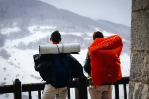 Two backpackers with hiking packs overlooking a snow-covered mountain landscape during a winter trek