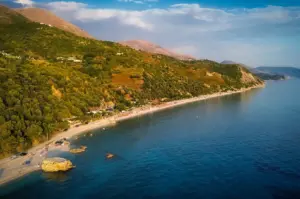 Aerial view of a scenic coastal beach with green mountains and blue sea