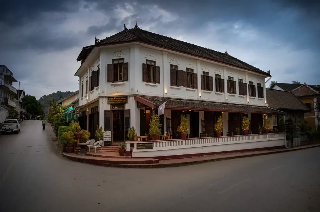 Traditional Luang Prabang Laos hotel with white colonial architecture, wooden shutters, ornate roof, veranda, and mountain views