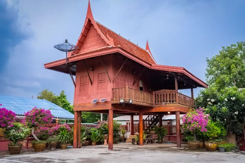 Traditional Thai wooden stilt house at Athithara Homestay in Ayutthaya, Thailand, surrounded by tropical gardens and flowering plants with classic Thai architecture.