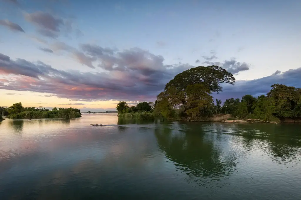 Mekong River in Laos at sunset with calm water, lush green islands, a traditional boat, and colorful clouds reflecting across the river