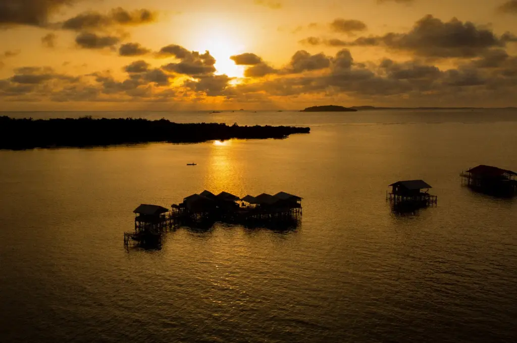 Sunset over the Riau Islands with traditional stilt houses on the sea and a golden coastal horizon