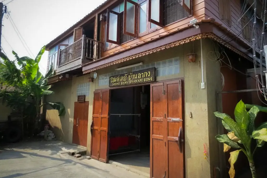 Entrance to Baan Are Gong Riverside Homestay in Ayutthaya, Thailand, featuring a traditional wooden guesthouse facade along a quiet local street with authentic Thai architecture.