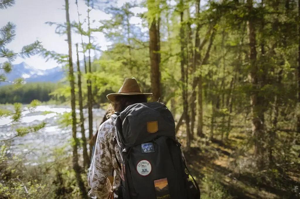 Backpacker with a large hiking backpack walking through a forest trail beside a river with mountains in the distance