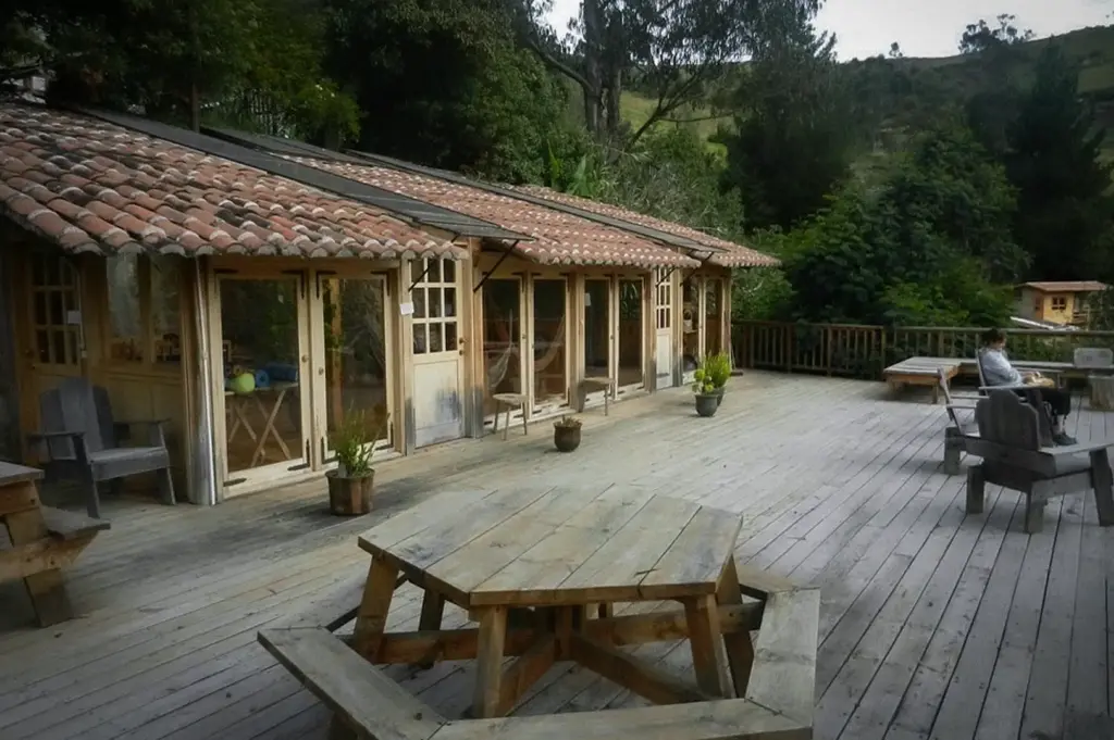 Spacious wooden deck at Black Sheep Inn Ecolodge featuring rustic cabins, outdoor seating, and scenic mountain views surrounded by lush greenery.