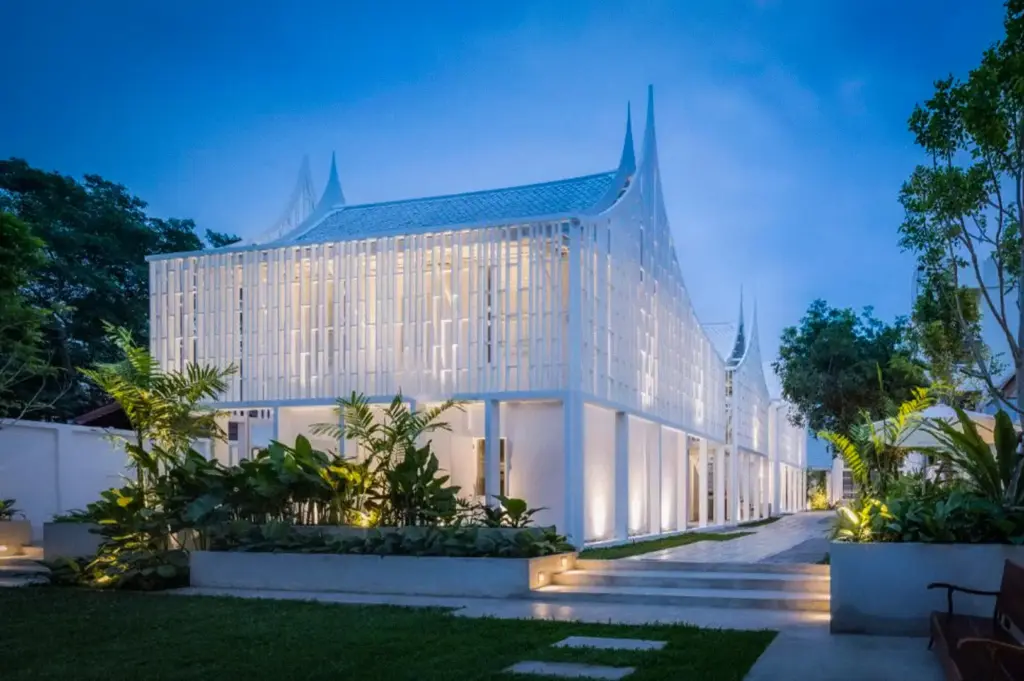 Modern white architectural exterior of Busaba Ayutthaya Hotel in Ayutthaya, Thailand, featuring contemporary Thai-inspired design, landscaped gardens, and illuminated evening ambiance.
