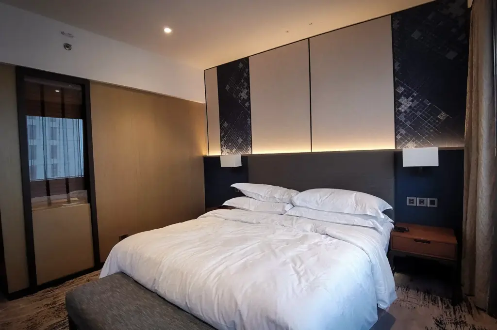 Modern hotel room with a neatly made bed, contemporary furnishings, bedside lighting, and warm interior design