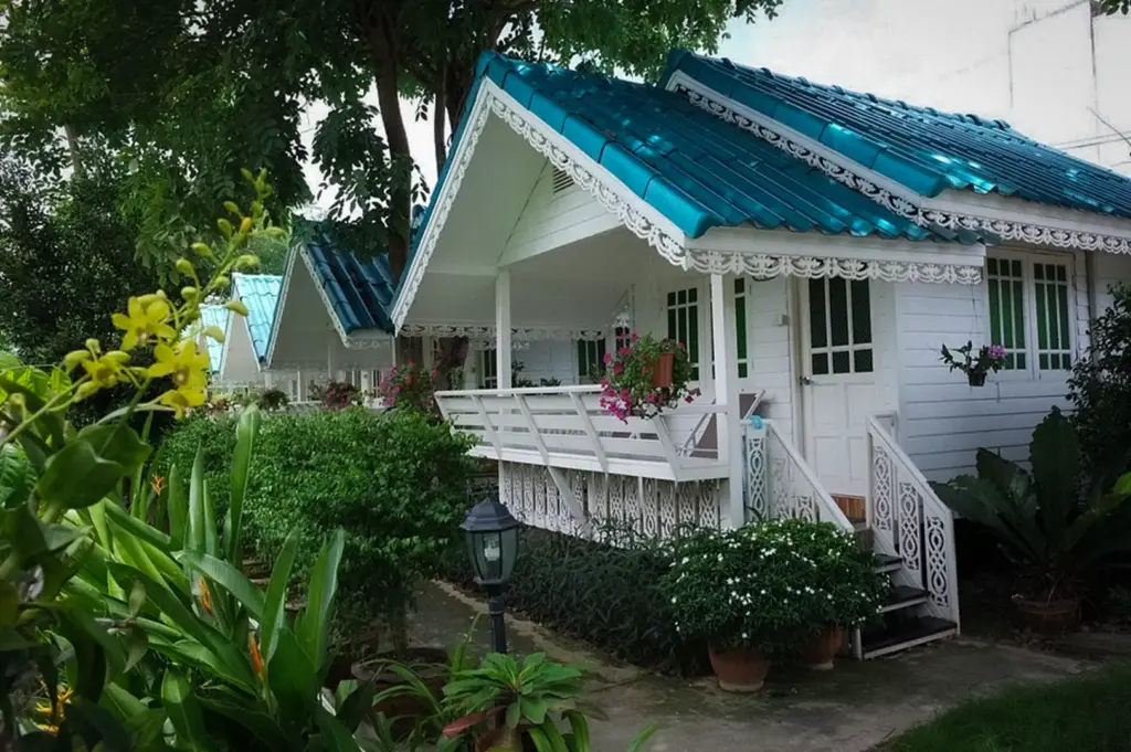 Traditional white wooden cottage at Baan Luang Harn in Ayutthaya, Thailand, surrounded by lush tropical gardens with classic Thai architecture and a peaceful resort atmosphere.