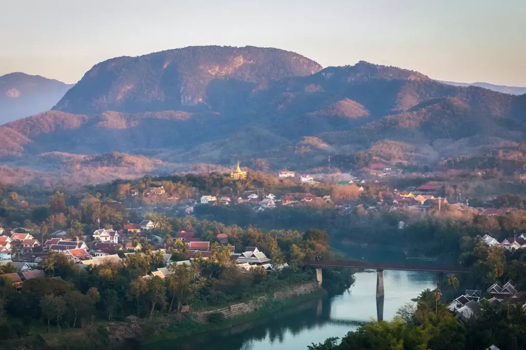 View from Mount Phou Si overlooking Luang Prabang with mountains, temples, rooftops, and river at sunset