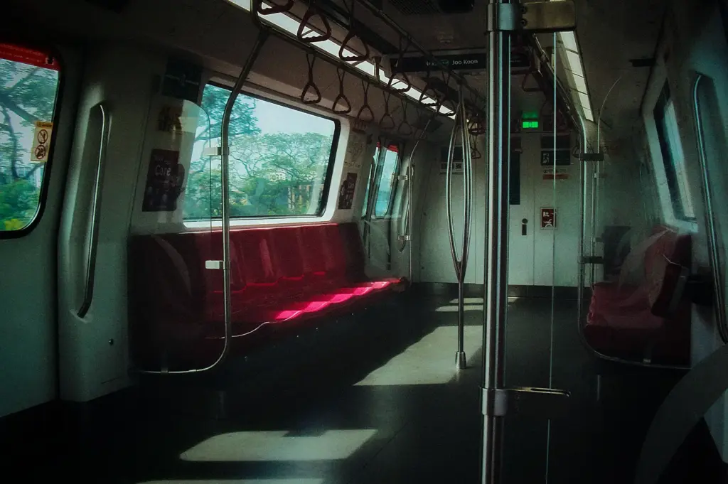 Quiet interior view of an empty Singapore MRT train carriage showing red seating, grab handles, and large viewing windows in soft sunlight.