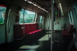 Quiet interior view of an empty Singapore MRT train carriage showing red seating, grab handles, and large viewing windows in soft sunlight.