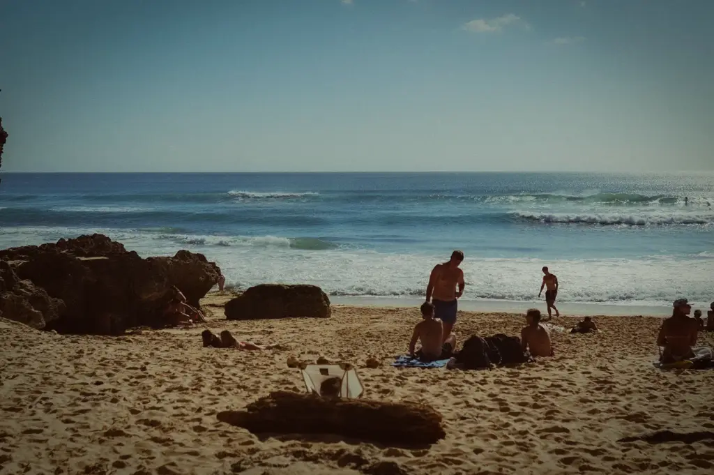 Tropical beach vacation with sandy shoreline, ocean waves, rocky coastline, and people relaxing by the sea.