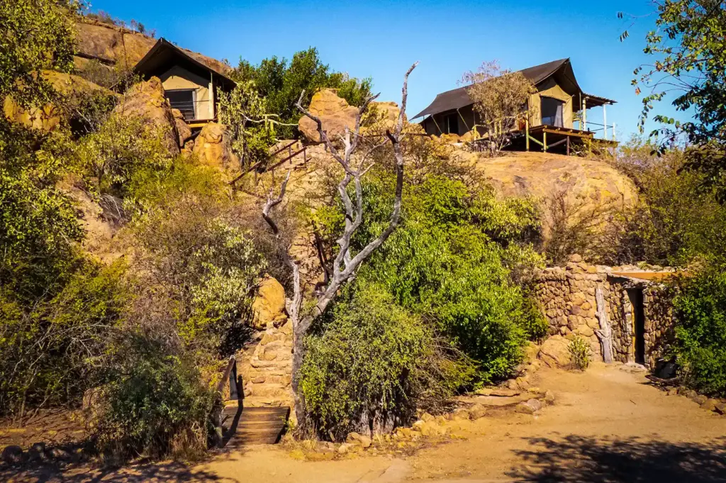 Eco lodge accommodations built among rocky hills, surrounded by trees, shrubs, and natural stone pathways.
