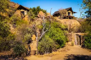 Eco lodge accommodations built among rocky hills, surrounded by trees, shrubs, and natural stone pathways.