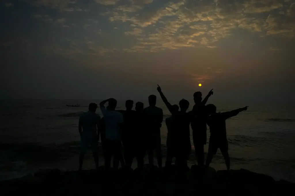 Silhouettes standing together on a rocky shoreline facing the ocean against a dramatic sunset sky.