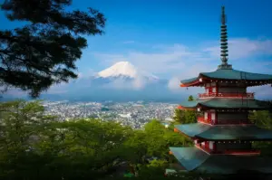 Iconic view of the red and green Chureito Pagoda overlooking Fujiyoshida city with the snow-capped Mount Fuji in the background under a blue sky.