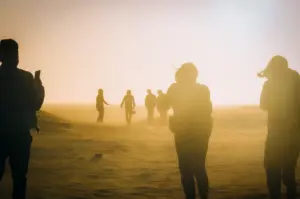 Group of travelers walking across a sandy desert landscape at sunset.