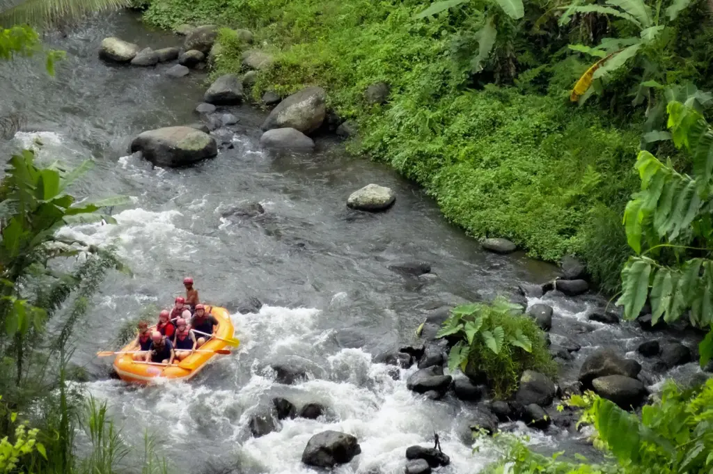 An overhead view of an orange raft navigating whitewater rapids down the lush Ayung River Valley near Ubud, Bali, Indonesia, surrounded by dense tropical foliage.