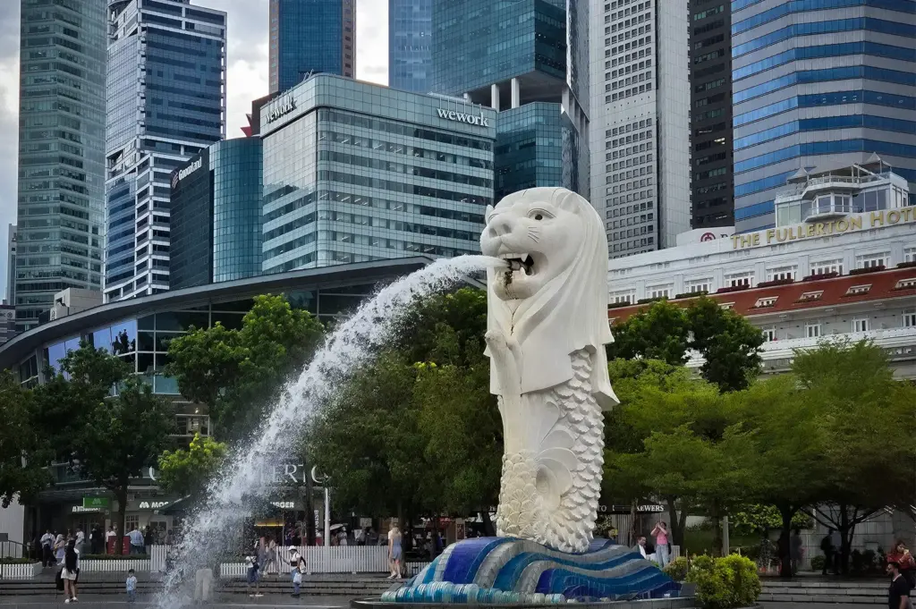 Merlion statue at Merlion Park in Singapore with water spraying from its mouth, surrounded by the Fullerton Hotel and Singapore's downtown skyline.