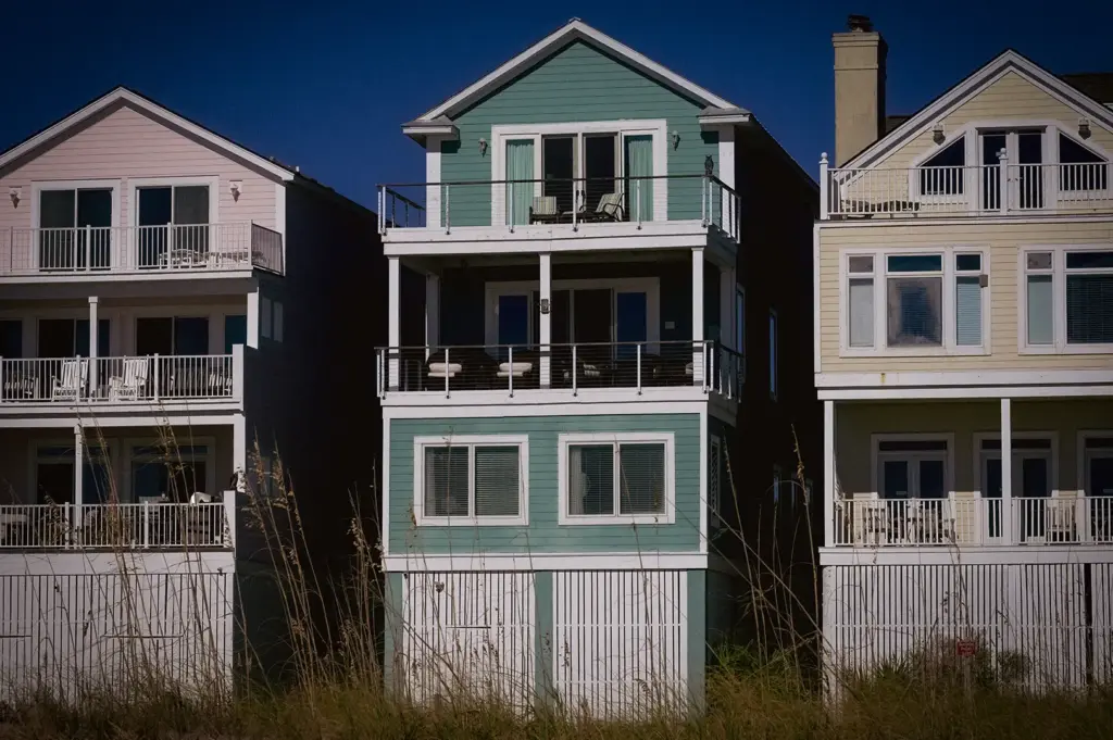 Row of multi-story beachfront holiday homes with balconies and gabled roofs situated behind coastal dune grass