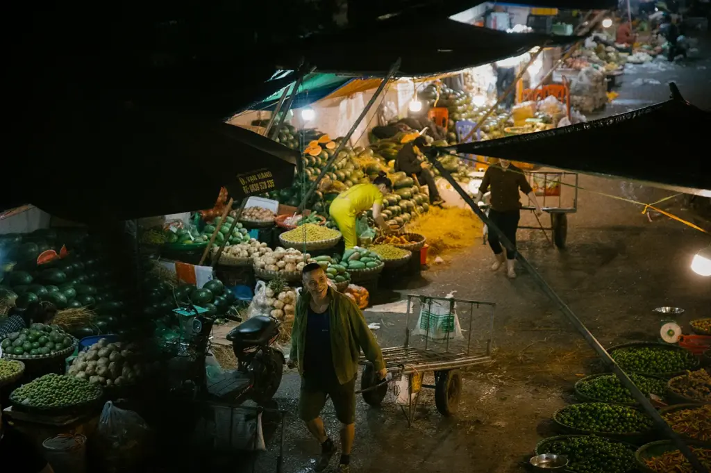 Busy outdoor market at night with fresh produce stalls, vendors, and shoppers.