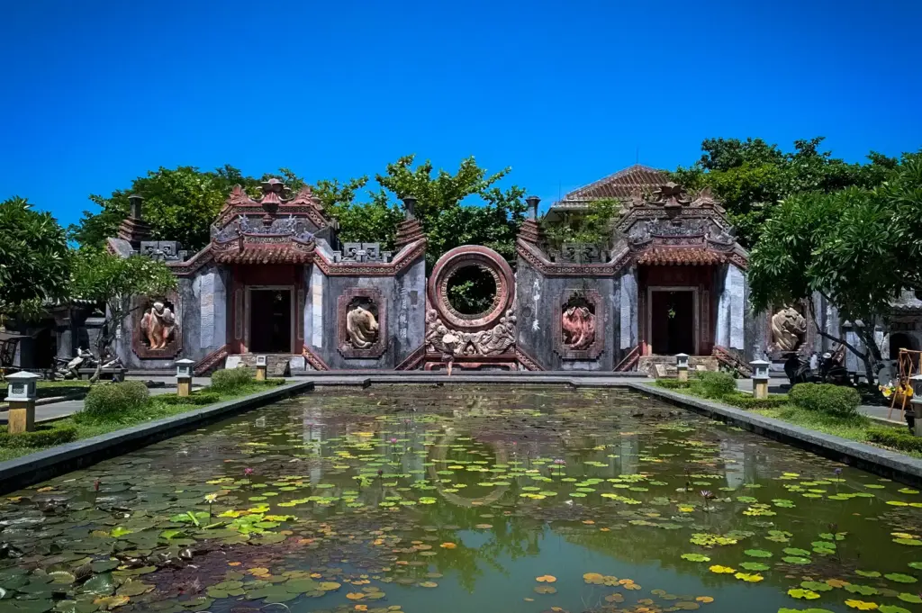Ba Mu Temple in Hoi An, Vietnam, featuring its ornate historic gate and a lotus-filled pond under a bright blue sky.