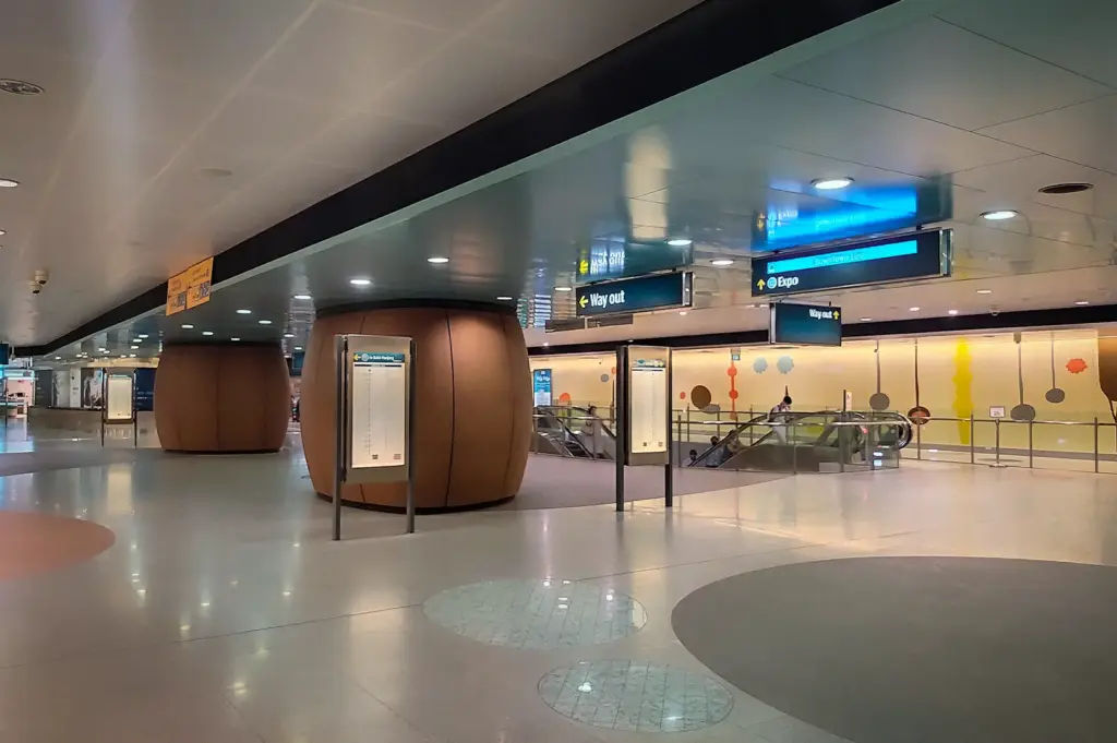 Telok Ayer MRT station concourse in Singapore with directional signs, escalators, and distinctive curved brown architectural columns.