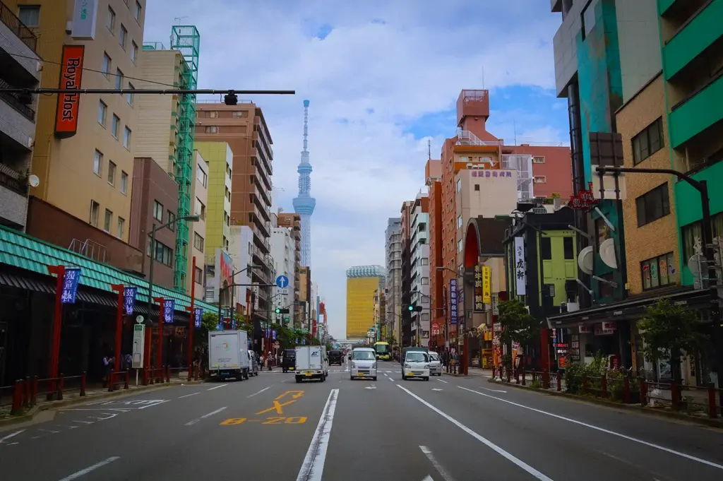 Busy Tokyo street view framed by urban buildings and storefronts with the Tokyo Skytree tower rising in the distance under a partly cloudy sky.