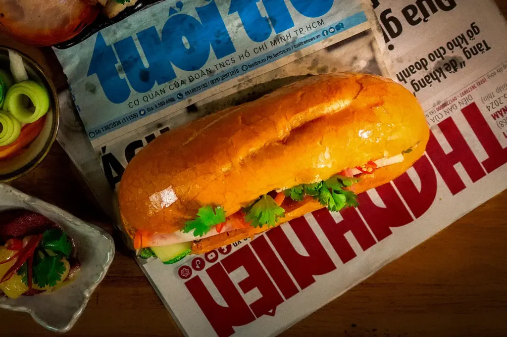 Vietnamese banh mi sandwich with a crispy baguette, pickled vegetables, fresh cilantro, cucumber, and chili served over a Vietnamese newspaper.