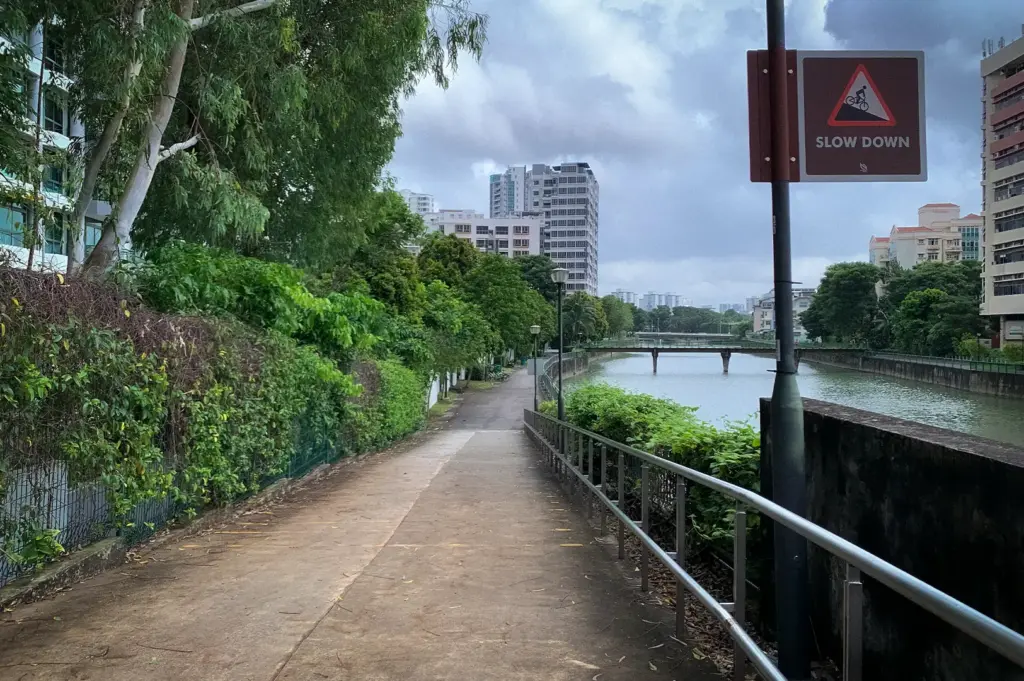 Kallang Park Connector in Bendemeer, Singapore, with a riverside walking path, lush greenery, and a cycling slow-down sign.
