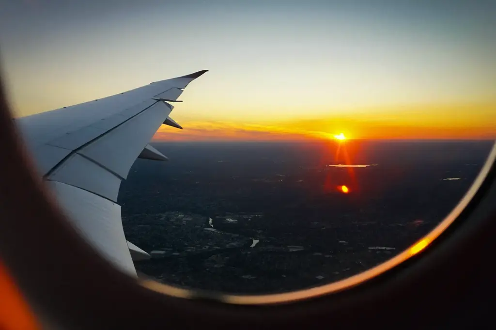 Scenic view from an airplane window capturing the aircraft wing cutting across a vibrant sunset sky on the horizon.