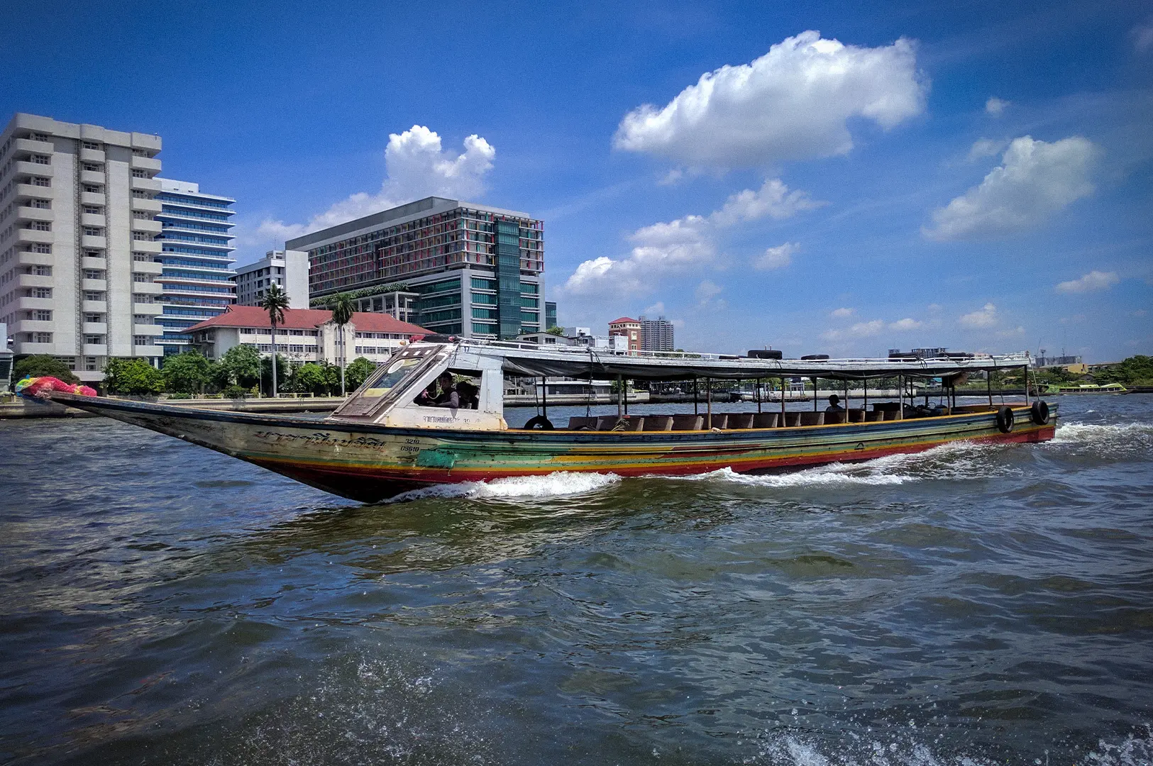 Chao Phraya River Bangkok with a traditional long-tail boat cruising past the city waterfront