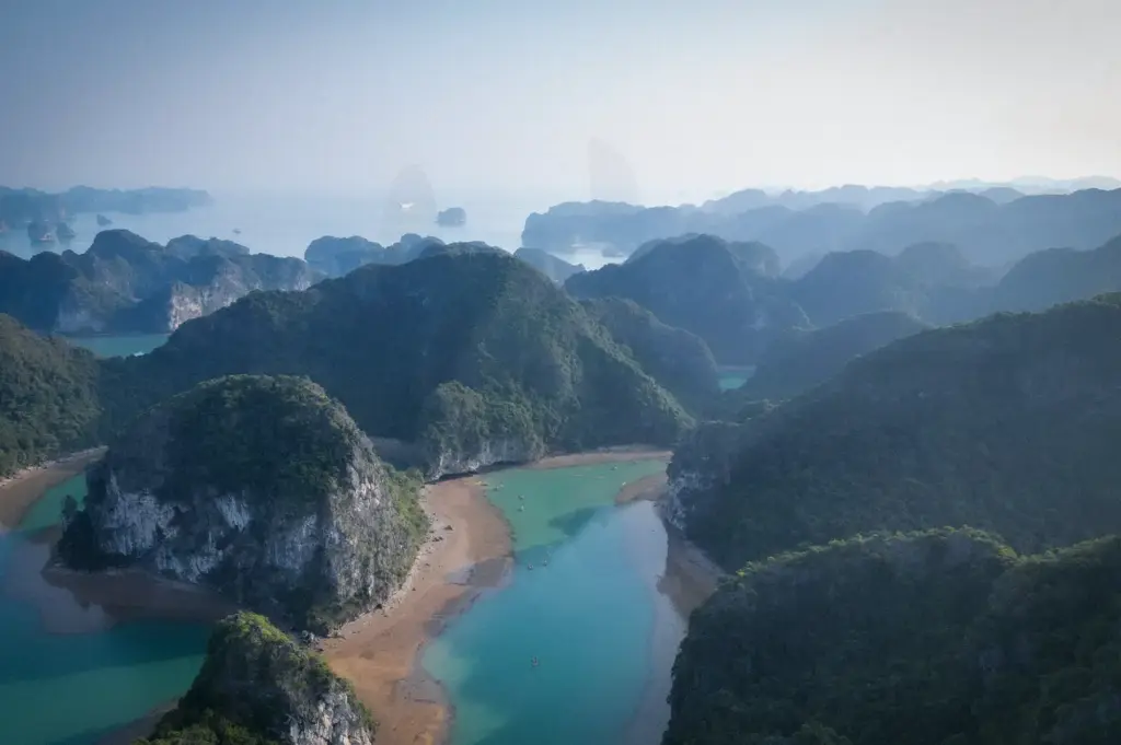 High-angle aerial view of emerald waters, sandy shores, and lush limestone karst islands in Ha Long Bay, Vietnam