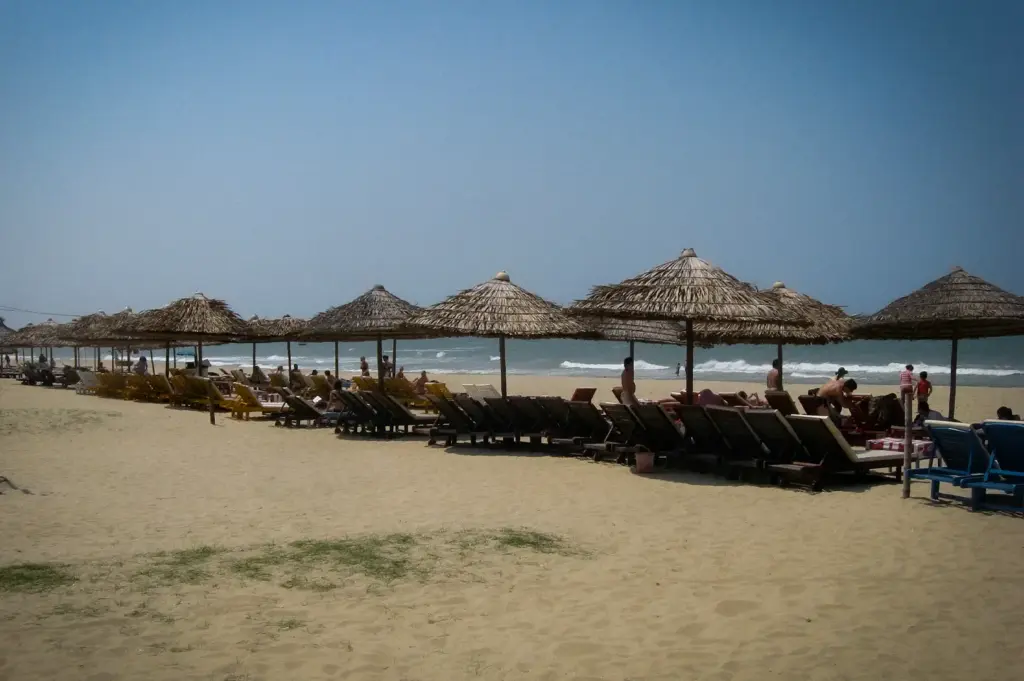 Row of thatched parasols and wooden sun loungers lined along the sandy shore at Cua Dai Beach in Hoi An, Vietnam