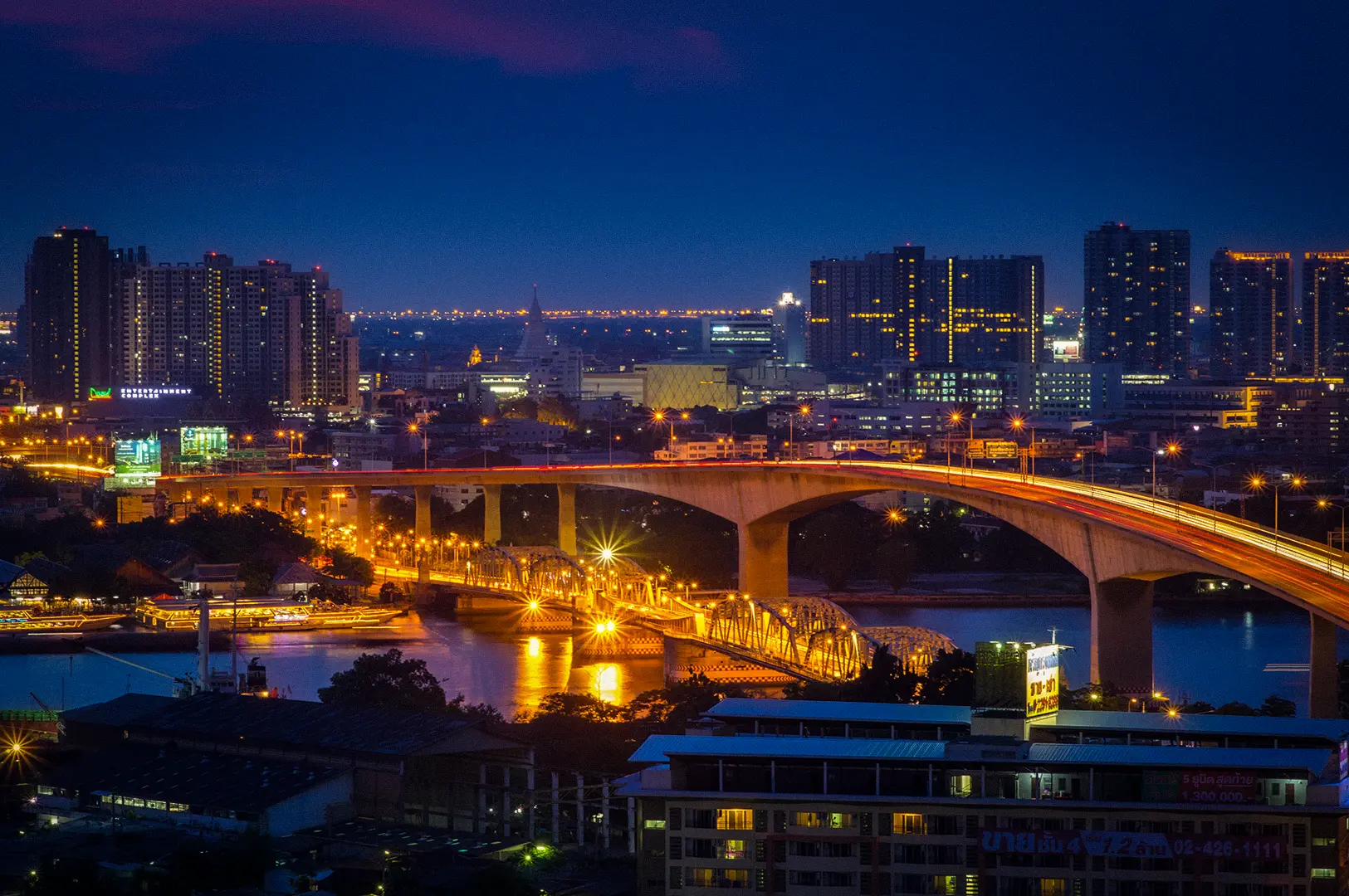 Bangkok city skyline at night with illuminated bridges, river reflections, and high-rise buildings