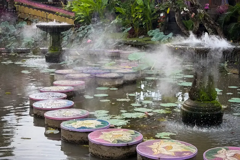Painted lotus stepping stones curving across a lush water pond with fountains and traditional shrines at Pura Taman Kemuda Saraswati (Ubud Water Palace) in Ubud, Bali, Indonesia.