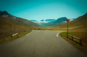 Scenic mountain road winding through a vast valley with snow-capped peaks in the background under a clear sky