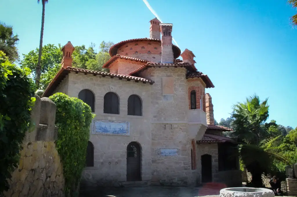 Detailed architectural view of the stone tower and terracotta roof of Villa Sassetti, surrounded by lush trees and greenery in Sintra, Portugal