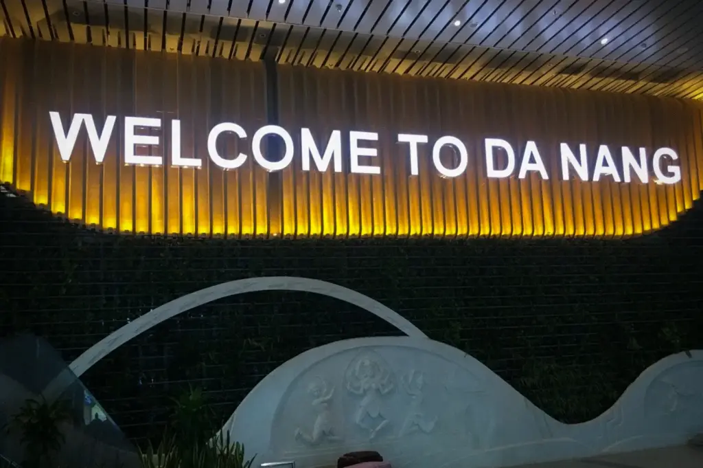 An illuminated Welcome to Da Nang sign with warm backlit slatted panels above decorative stone carvings and green feature wall inside Da Nang International Airport