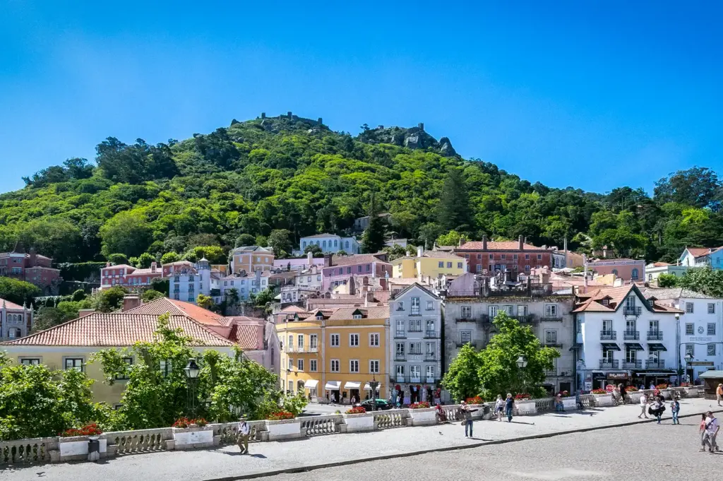 Historic town square and colorful buildings in Sintra, Portugal, set against a lush green hill under a clear blue sky