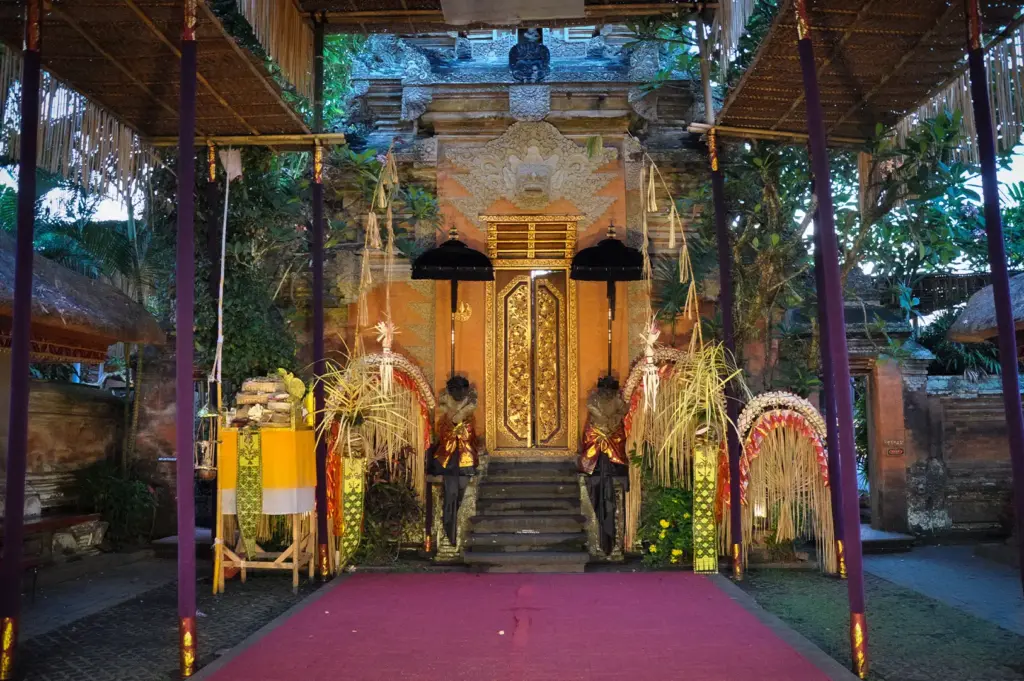 An interior courtyard view of Ubud Palace in Bali, featuring a traditional ornate golden gateway entrance, ceremonial decorations, and a red carpet path.