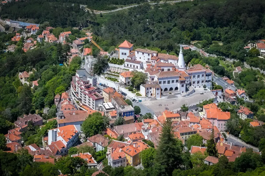 Aerial view of the National Palace of Sintra with its iconic twin conical chimneys, surrounded by the historic town and lush green hills of Portugal