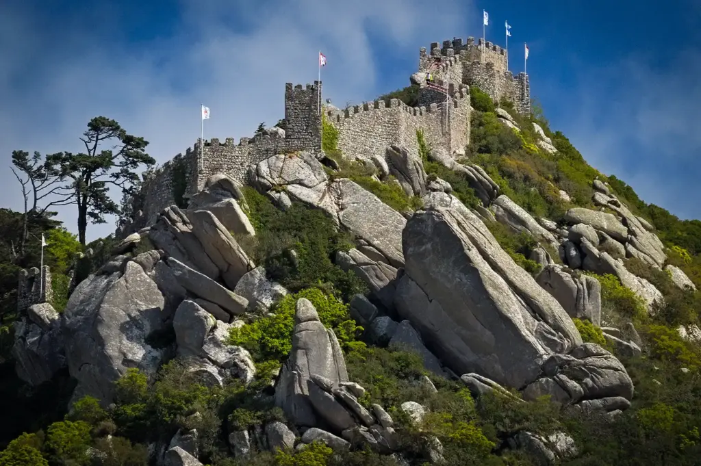 Muralhas de pedra e torres defensivas históricas do Castelo dos Mouros serpenteando por encostas rochosas e arborizadas em Sintra, Portugal