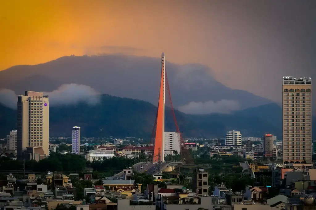 Aerial view of the cable-stayed Tran Thi Ly Bridge spanning the Han River against a sunset sky and mountain backdrop in Da Nang