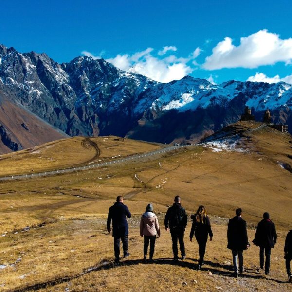 A group of friends walking together on a scenic mountain trail, surrounded by lush greenery and rocky terrain.